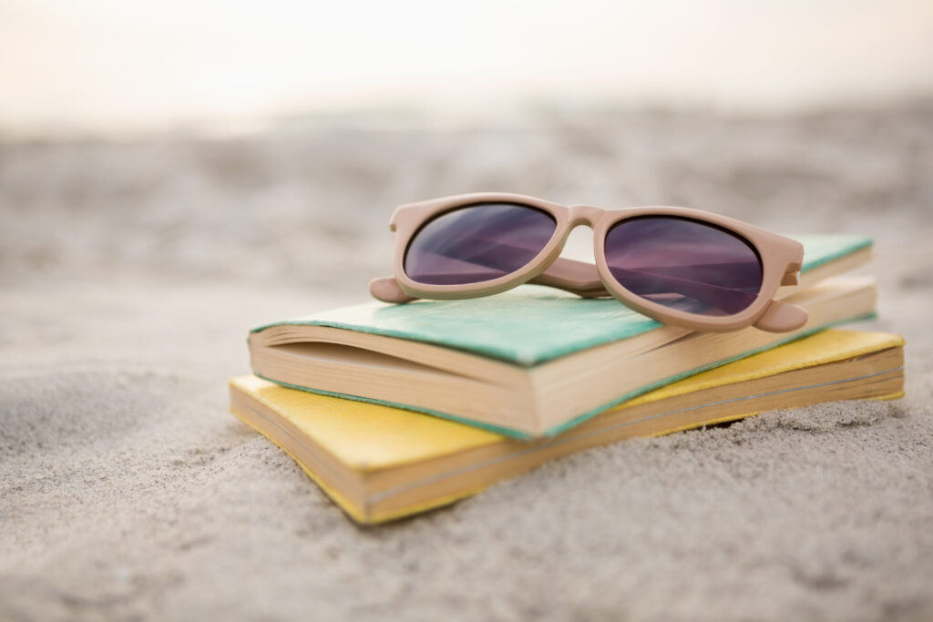 <p>Sunglasses and books on sand at beach</p>
